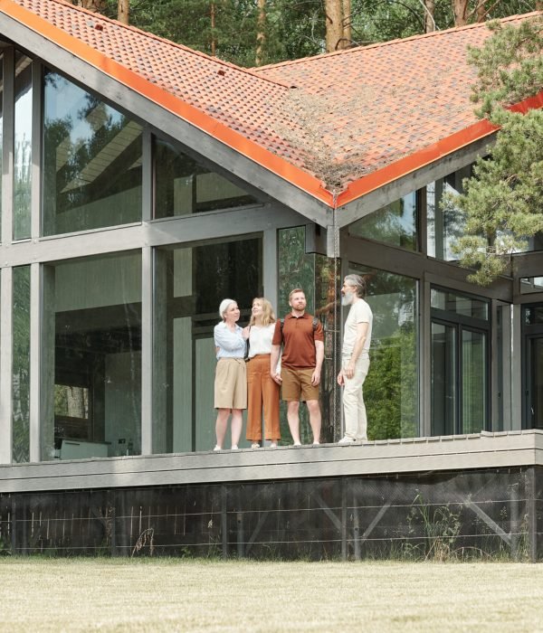 Young daughter and son standing with senior parents against beautiful cottage and contemplating nature around