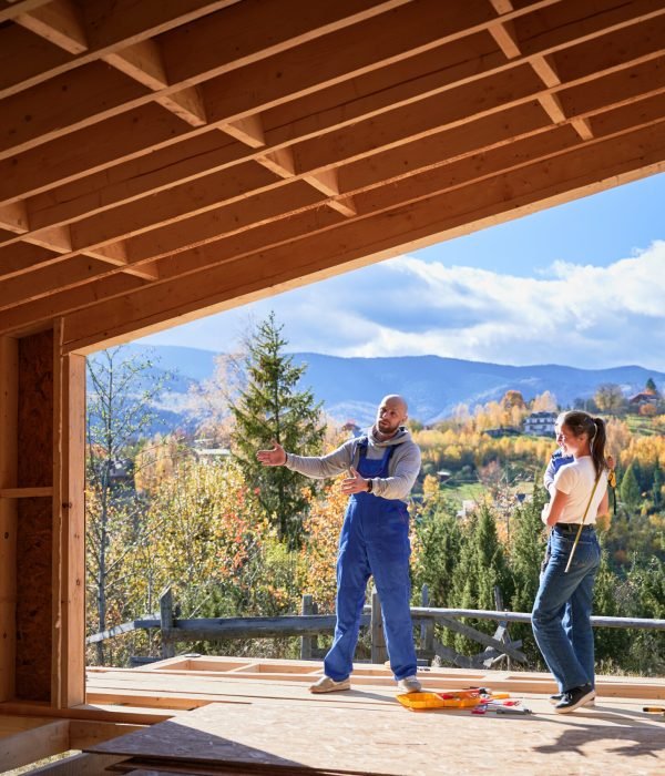 Father, mother and son building wooden frame house. Male designer in blue overalls showing future home, standing on terrace on construction site. Carpentry, family concept.